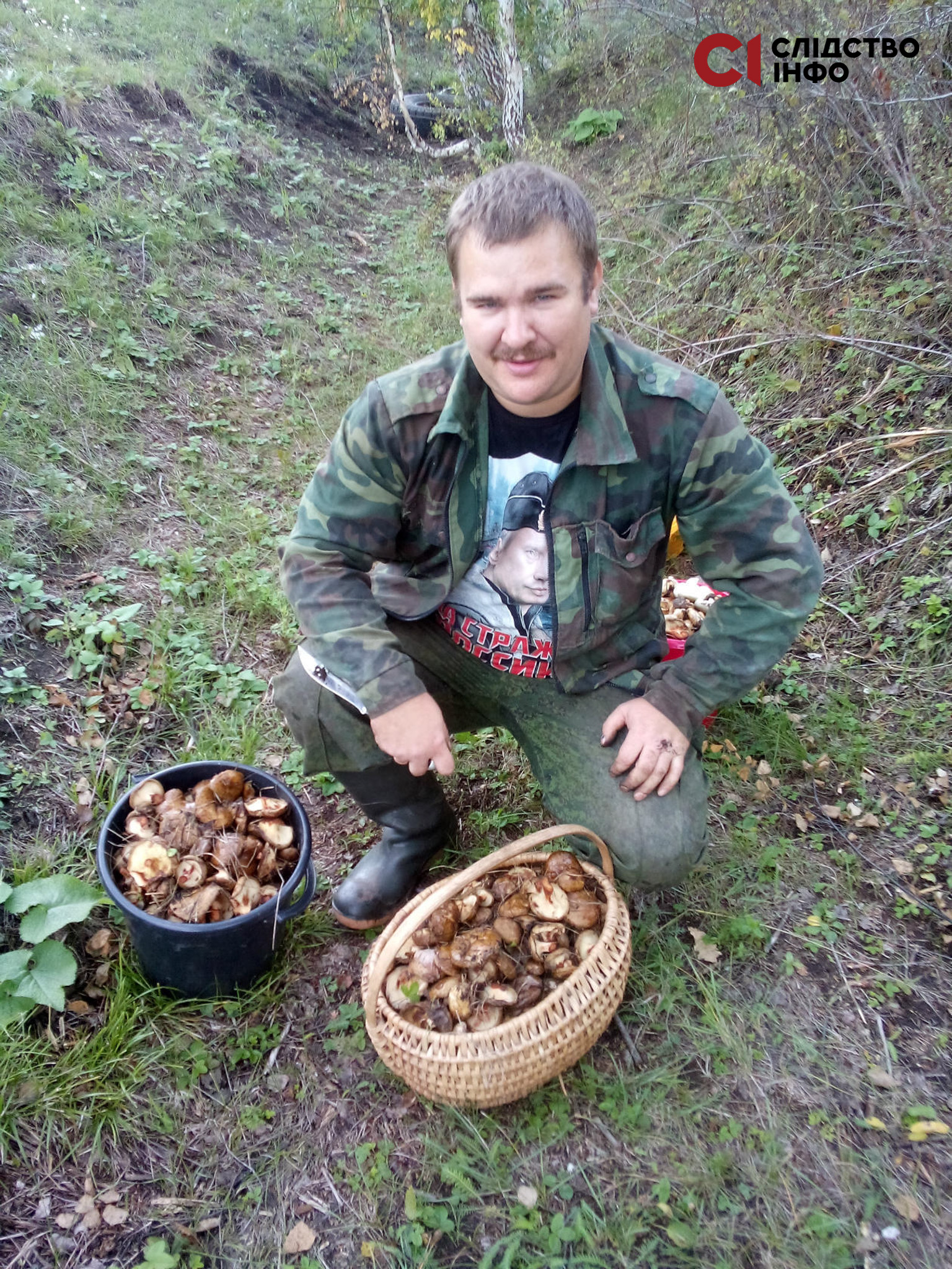 Чоловік сидить навшпиньки на природі, біля нього чорне відро і світлий кошик, наповнені грибами