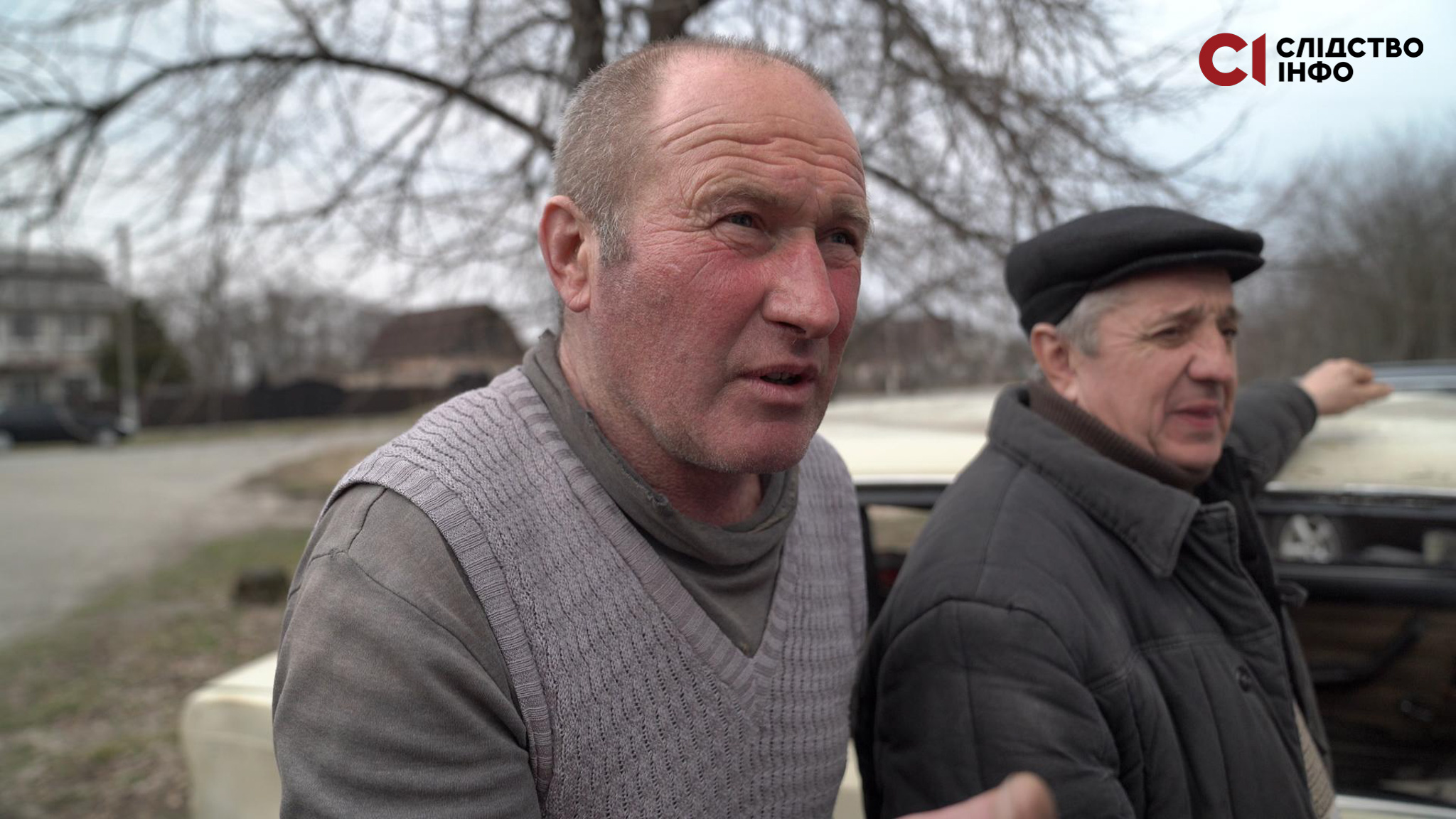 На фото два чоловіки стоять біля світлого авто