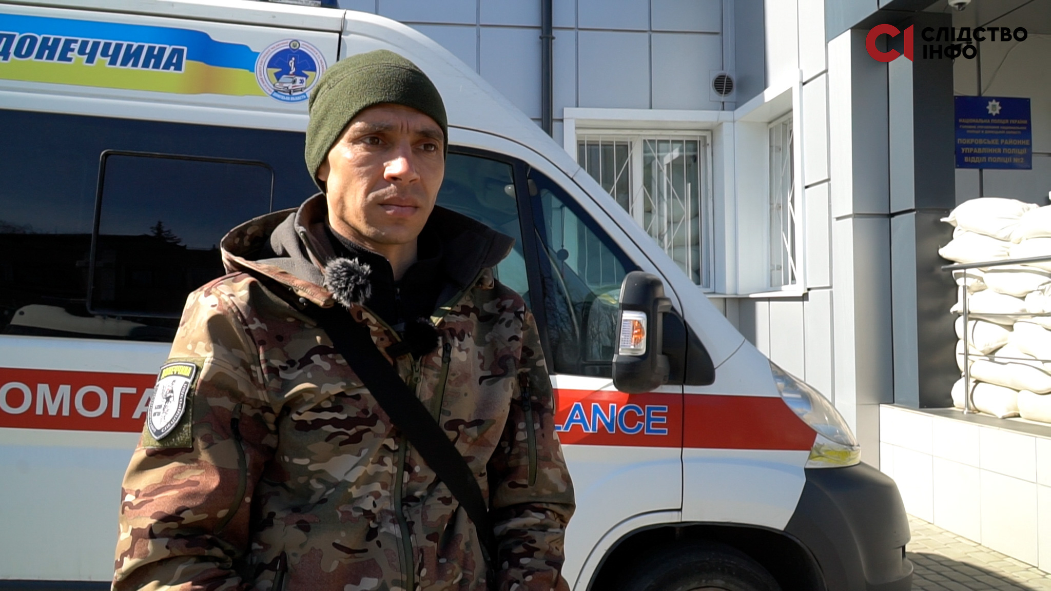 На фото чоловік у військовій формі стоїть на фоні швидкої допомоги