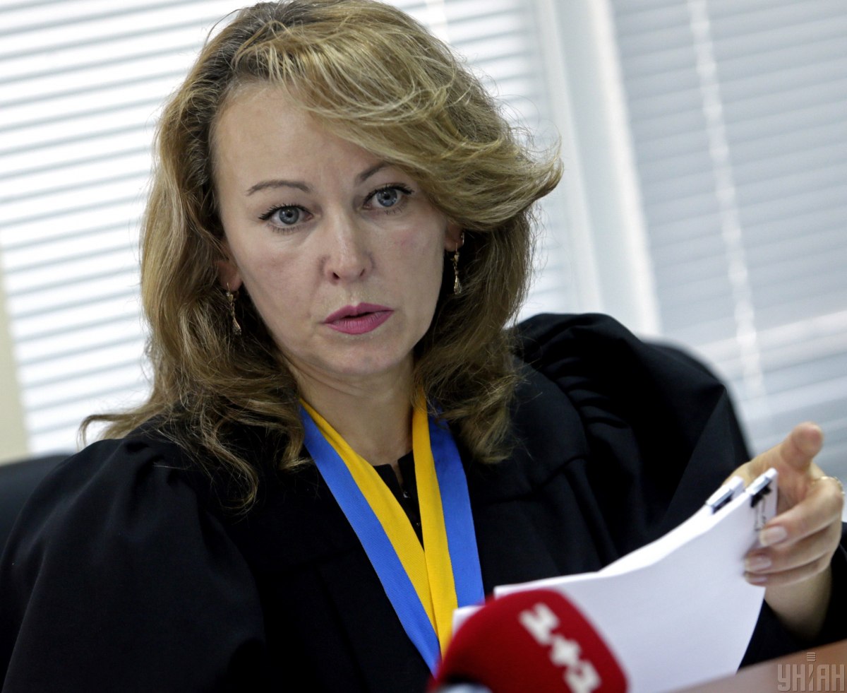 Портретне фото жінки-судді у мантії, на шиї висить синьо=жовта стрічка, у руках жінка тримає папери формату А4