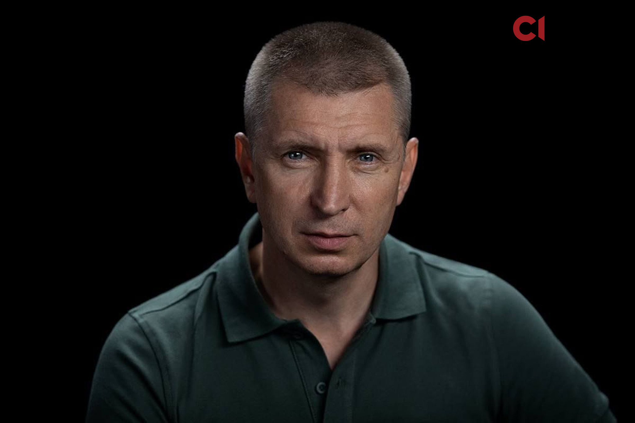 На чорному фоні зображено портретне фото чоловіка з короткою стрижкою у зеленому поло