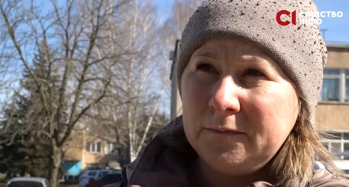 На фото крупним планом лице жінки у шапці, яка стоїть на фоні дерев і будівлі