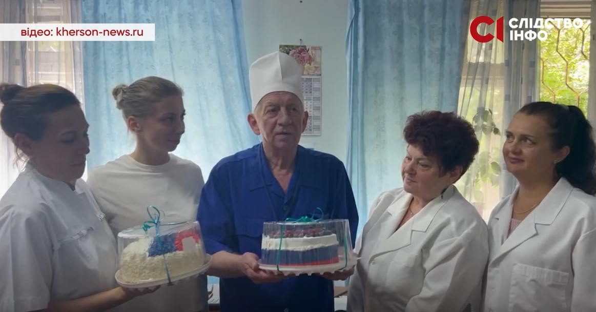На фото п'ятеро людей чотири жінки в білих халатах і по центру чоловік у синьому лікарському костюмі й білому головному уборі. Чоловік тримає торт у кольорах прапора Росії.