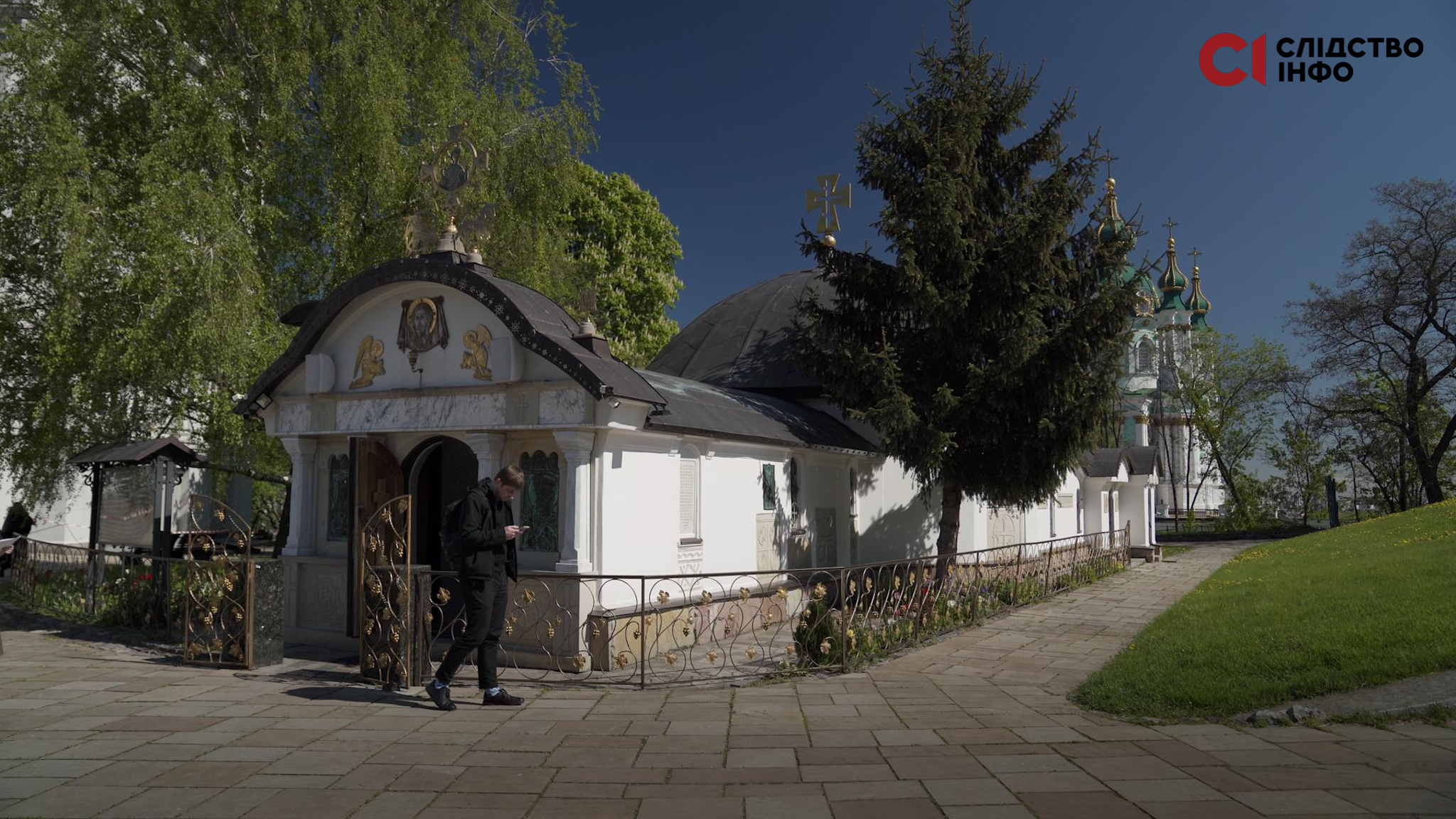 На фото церква стоїть між дерев, світить сонце.