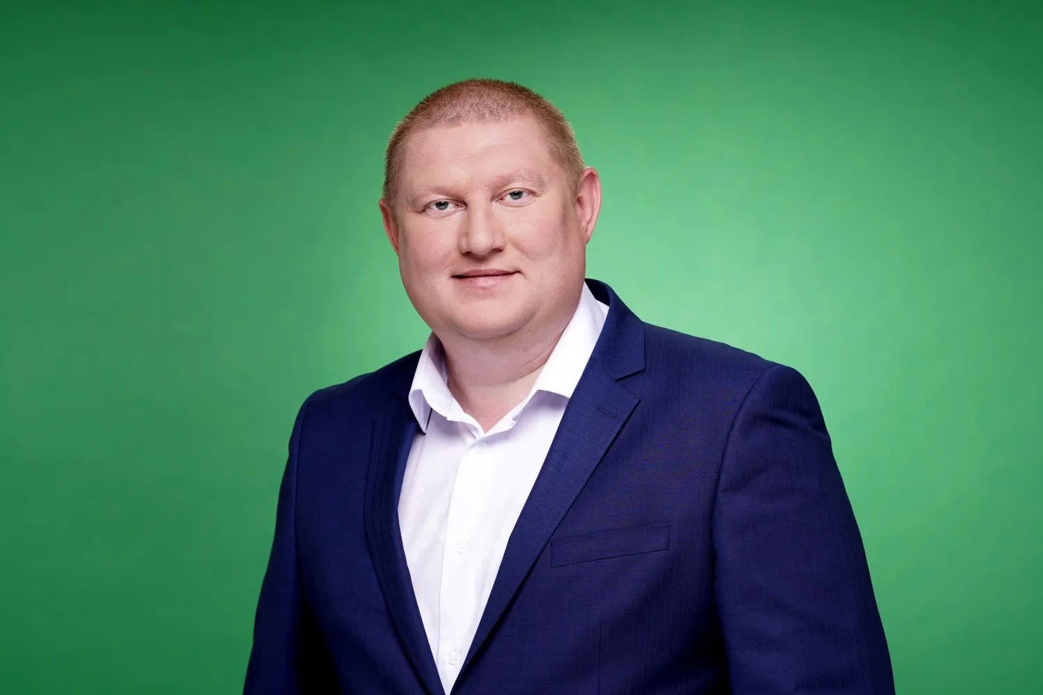 Чоловік у білій сорочці й темно-синьому піджаку стоїть на зеленому фоні