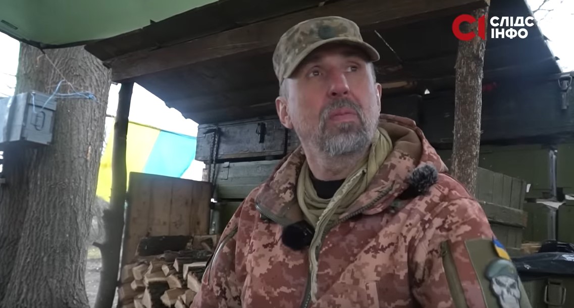 На фото український військовий сидить у бліндажі й дивиться праворуч