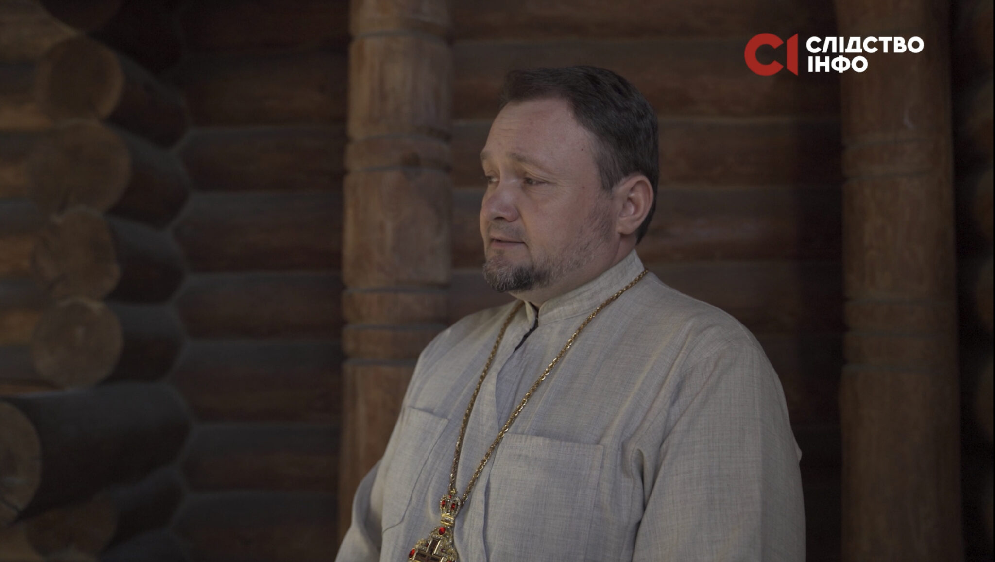 На фото настоятель церкви у світлому одязі з позолоченим хрестом на шиї. Позад нього дерев'яні стіни